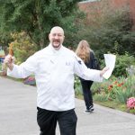 Aaron Guerra in chef's jacket, smiling, with arms lifted