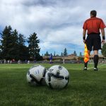referee looking with back turned to camera, two soccer balls in foreground