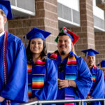 Students line up to receive diplomas. Two students look directly at the camera smiling.
